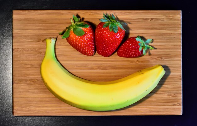 Vista de ángulo alto de un plátano con fresas en la tabla de cortar