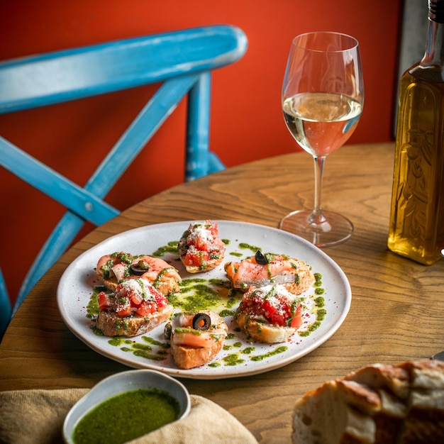 Foto vista de ángulo alto de rebanadas de pan con pescado y tomates en plato blanco un vaso de vino blanco un vaso de aceite de oliva en la mesa de madera