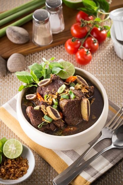 Vista de ángulo alto de la sopa de konro servida en un cuenco con tenedor y cuchara en la mesa