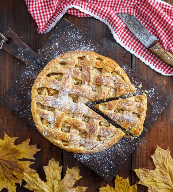 Foto vista de ángulo alto de la tarta de manzana en la tabla de cortar por las hojas de otoño