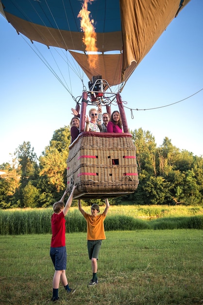 Foto vista de ángulo bajo de amigos volando en globo de aire caliente mientras los niños están de pie en el campo de hierba