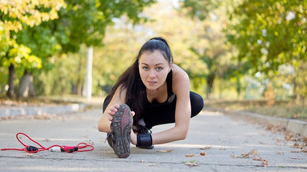 Foto vista de ángulo bajo de una atleta joven y atractiva que se extiende con la pierna extendida cerca de la superficie de la carretera mientras se calienta para su entrenamiento y entrenamiento