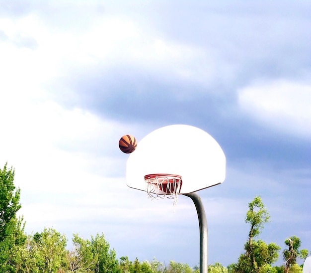Vista de bajo ángulo de baloncesto y aro contra el cielo nublado