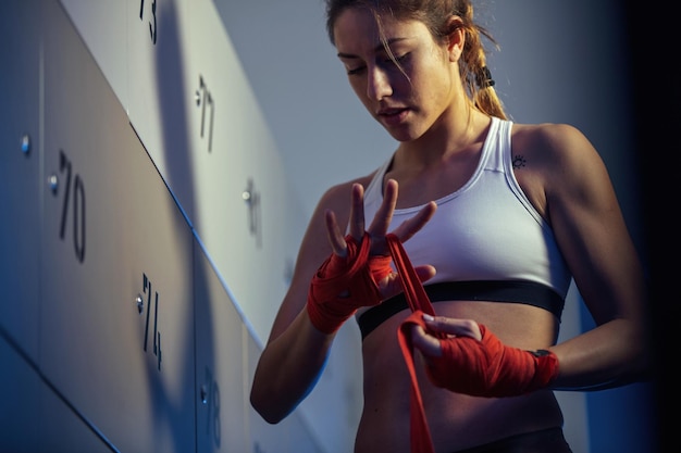 Vista de ángulo bajo de la boxeadora vendando sus manos en el vestuario antes del entrenamiento deportivo