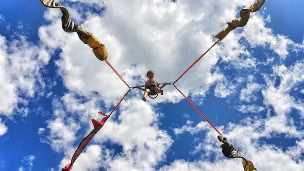 Vista de ángulo bajo de una chica sentada en un columpio de cadena en contra del cielo