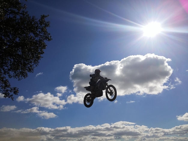 Vista de ángulo bajo de un corredor de motocross realizando una acrobacia en el aire contra el cielo
