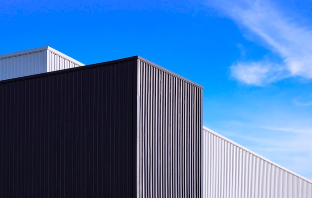 Vista de ángulo bajo de edificios de fábrica de metal corrugado en blanco y negro sobre fondo de cielo azul
