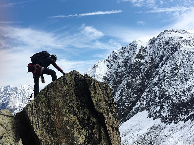 Foto vista de ángulo bajo de un excursionista masculino escalando un acantilado contra el cielo durante el invierno