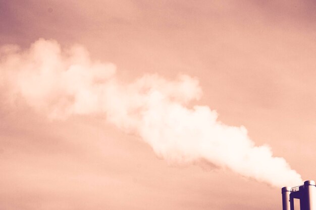 Foto vista de bajo ángulo de la fábrica emitiendo humo en el cielo durante la puesta del sol