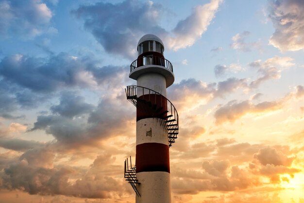 Vista de bajo ángulo del faro contra un cielo nublado durante la puesta de sol