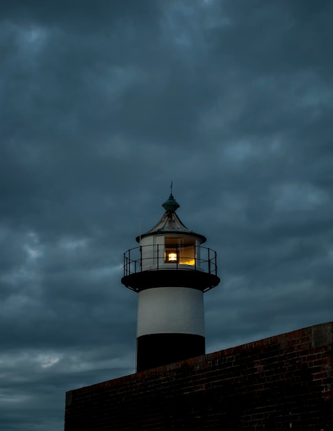 Foto vista de bajo ángulo del faro iluminado contra un cielo nublado