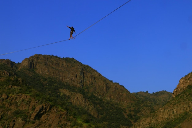 Vista de ángulo bajo de un hombre caminando en slackline sobre las montañas contra un cielo despejado