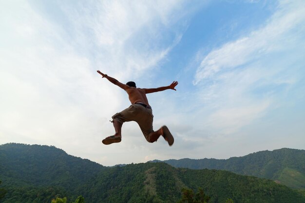 Foto vista de ángulo bajo de un hombre sin camisa saltando contra las montañas y el cielo