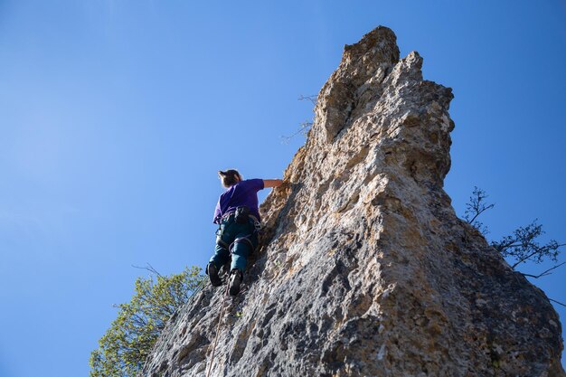 Vista de ángulo bajo de un hombre escalando roca contra el cielo.