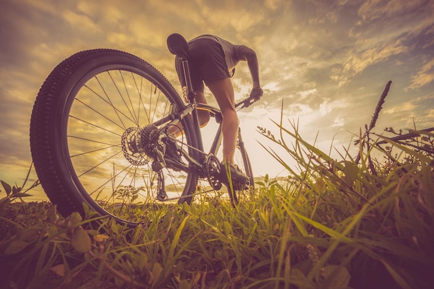 Vista de ángulo bajo de un hombre maduro montando una bicicleta en un campo cubierto de hierba contra un cielo nublado