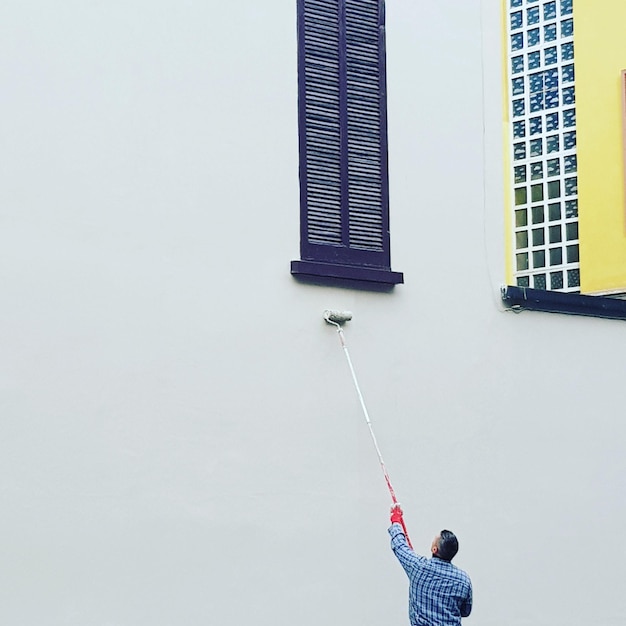 Foto vista en bajo ángulo de un hombre pintando una pared blanca