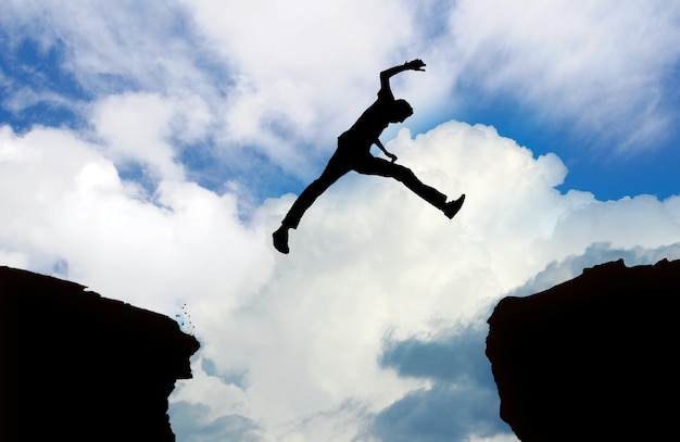 Foto vista de ángulo bajo de hombre silueta saltando en la roca contra el cielo