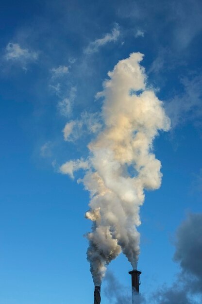 Foto vista en bajo ángulo del humo que emite la chimenea contra el cielo azul