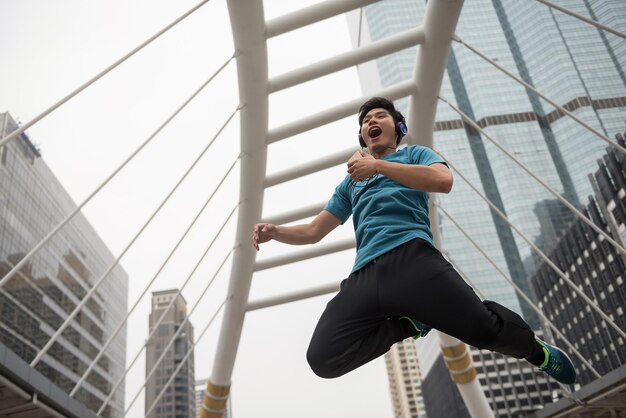 Foto vista de ángulo bajo de un joven alegre saltando mientras escucha música contra un edificio