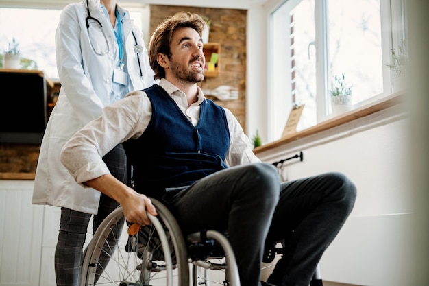 Vista de ángulo bajo de un joven discapacitado en silla de ruedas con una doctora en casa
