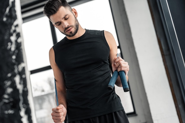 Vista de ángulo bajo del joven musculoso en ropa deportiva con cuerda de saltar en el gimnasio