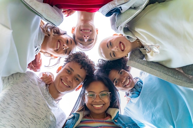 Vista de ángulo bajo de jóvenes amigos de moda abrazándose sonriendo y haciendo un círculo con la cabeza