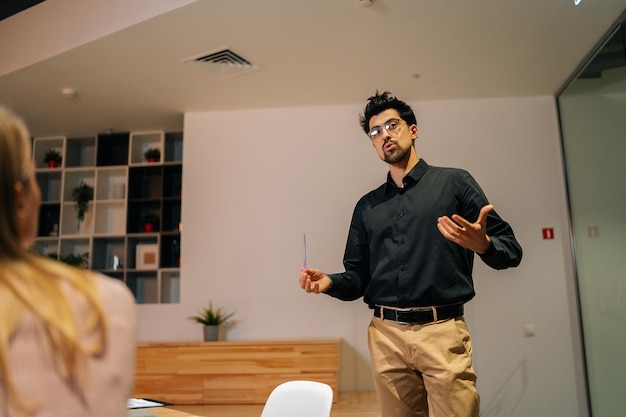 Vista de ángulo bajo del líder del equipo de negocios masculino que presenta el plan del proyecto a un grupo multiétnico que explica las tareas que hablan en la mesa en la reunión de la oficina