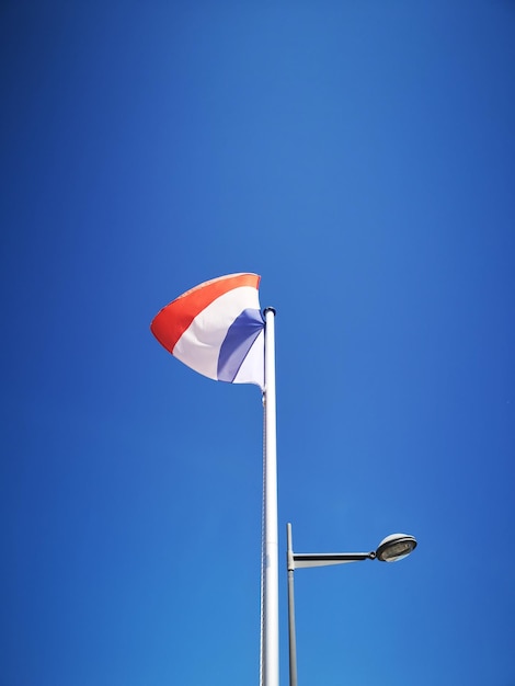 Foto vista de ángulo bajo de la luz de la calle contra un cielo azul claro y la bandera francesa