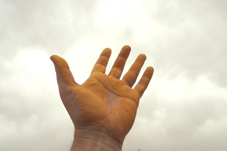 Foto vista de ángulo bajo de la mano humana con pintura amarilla contra el cielo nublado