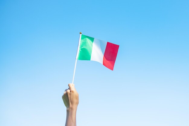 Vista de ángulo bajo de la mano sosteniendo la bandera contra un cielo azul claro