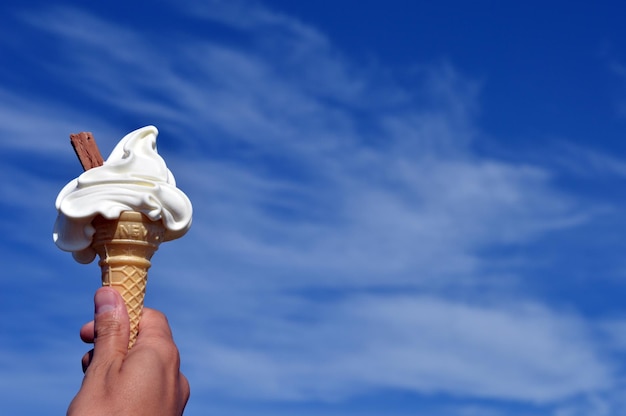 Vista de ángulo bajo de la mano sosteniendo helado contra el cielo azul