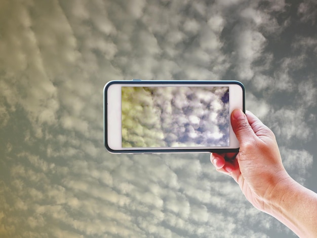 Vista de ángulo bajo de la mano sosteniendo el teléfono móvil contra el cielo nublado