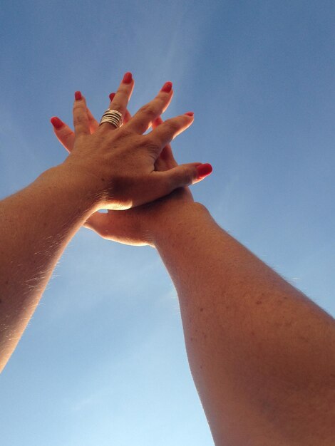 Foto vista de ángulo bajo de manos con esmalte de uñas rojo contra un cielo azul claro