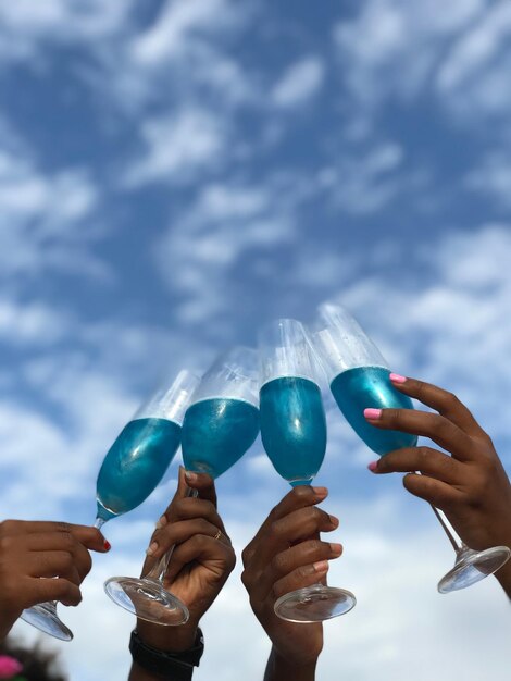 Foto vista de ángulo bajo de manos recortadas brindando copas contra el cielo