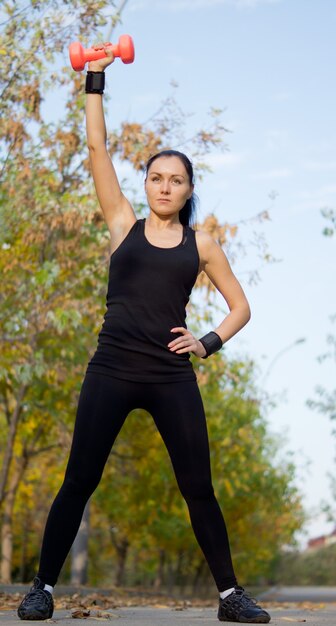 Vista de ángulo bajo de una mujer atlética en forma haciendo ejercicio con una mancuerna levantando su brazo por encima de su cabeza