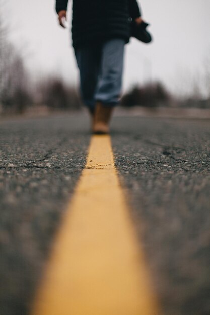 Vista de ángulo bajo de una mujer caminando a lo largo de la línea amarilla en la carretera