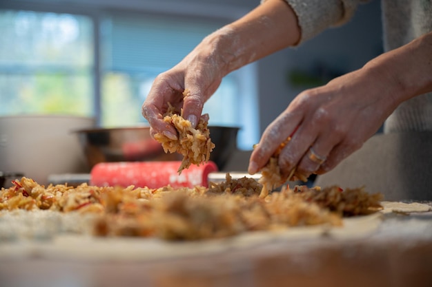 Vista de ángulo bajo de una mujer haciendo strudel de manzana casero tradicional dejando caer el relleno sobre una masa de hojaldre enrollada