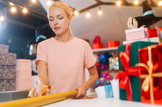 Vista de ángulo bajo de mujer joven cortando con tijeras envolviendo papel dorado para empaquetar festivo