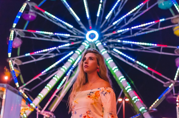 Foto vista de ángulo bajo de una mujer joven de pie contra la rueda de la ferris iluminada en un parque de atracciones