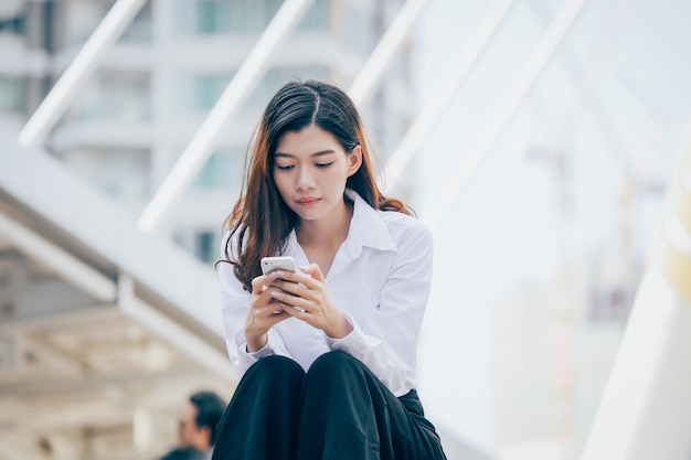 Vista de ángulo bajo de una mujer joven usando el teléfono móvil mientras está sentada al aire libre