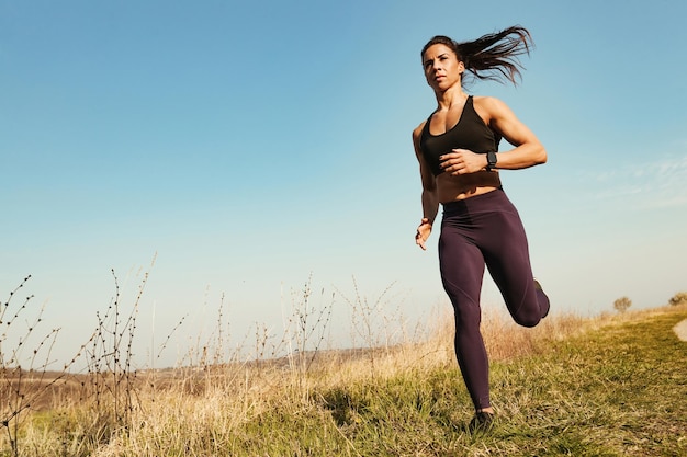 Vista de ángulo bajo de una mujer musculosa que tiene entrenamiento deportivo y corre en la naturaleza Copiar espacio