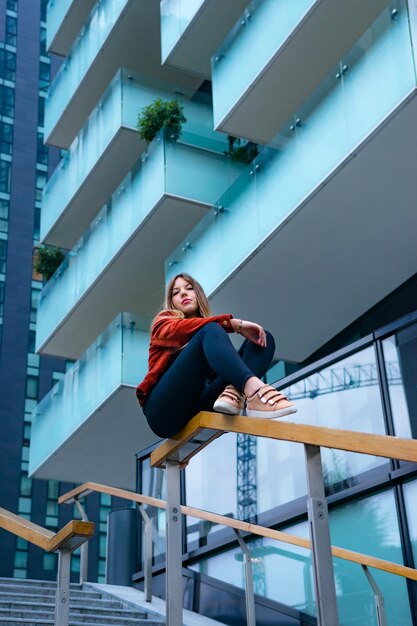 Foto vista de ángulo bajo de una mujer sentada en la barandilla contra un edificio en la ciudad