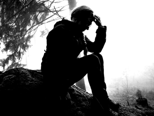 Vista de ángulo bajo de una mujer triste sentada en una roca contra el cielo