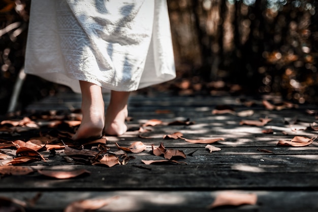Foto vista de ángulo bajo de mujer en vestido blanco caminando descalzo en el bosque oscuro