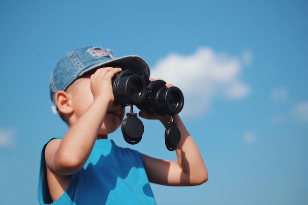 Vista de bajo ángulo de un niño fotografiando contra el cielo azul
