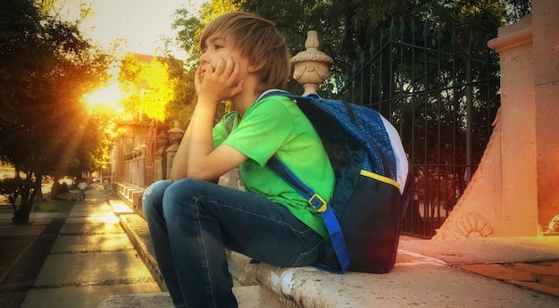 Vista de ángulo bajo de un niño sentado con las manos en la barbilla en el asiento al aire libre