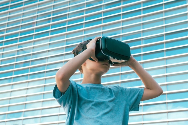 Vista de ángulo bajo de un niño usando un simulador de realidad virtual contra un edificio