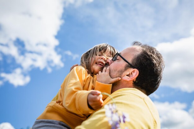 Foto vista de ángulo bajo de padre que está besando a su hija riendo.