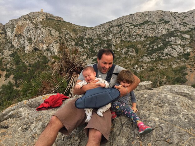 Vista de bajo ángulo de un padre sosteniendo a sus hijas en una formación rocosa