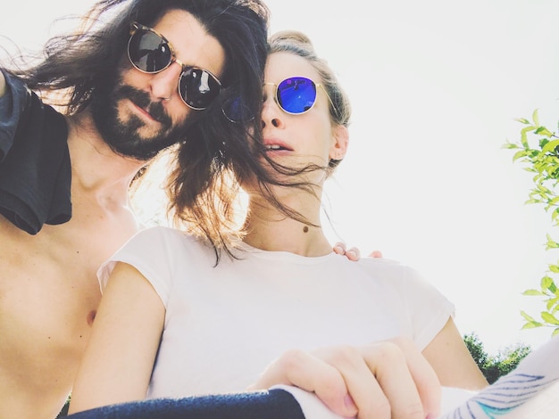 Vista de ángulo bajo de una pareja joven con gafas de sol sentada contra el cielo